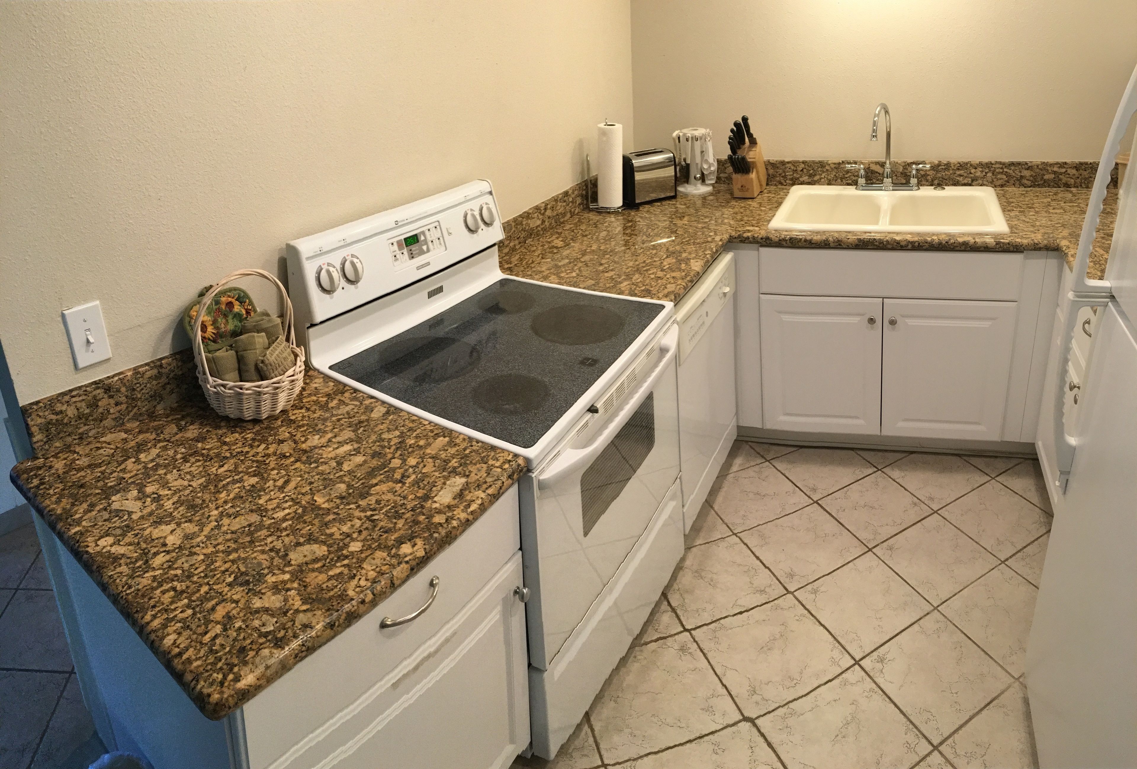 A kitchen with a granite countertop, white cabinets, a built-in oven, and a sink.