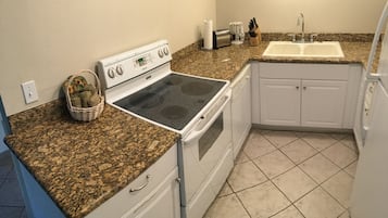 A kitchen with a granite countertop, white cabinets, a built-in oven, and a sink.