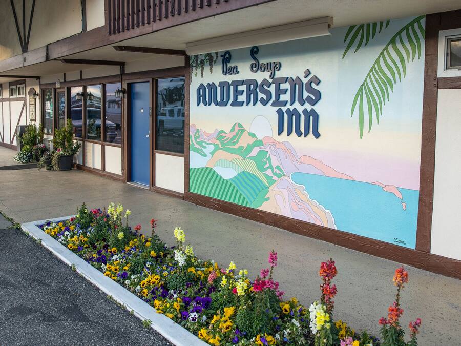 Un motel con un colorido mural en la pared exterior, un parterre de flores en la parte delantera y una vista despejada del estacionamiento.