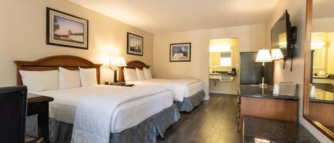 Habitación de hotel con dos camas, un escritorio, una silla, televisión y baño con espejo.