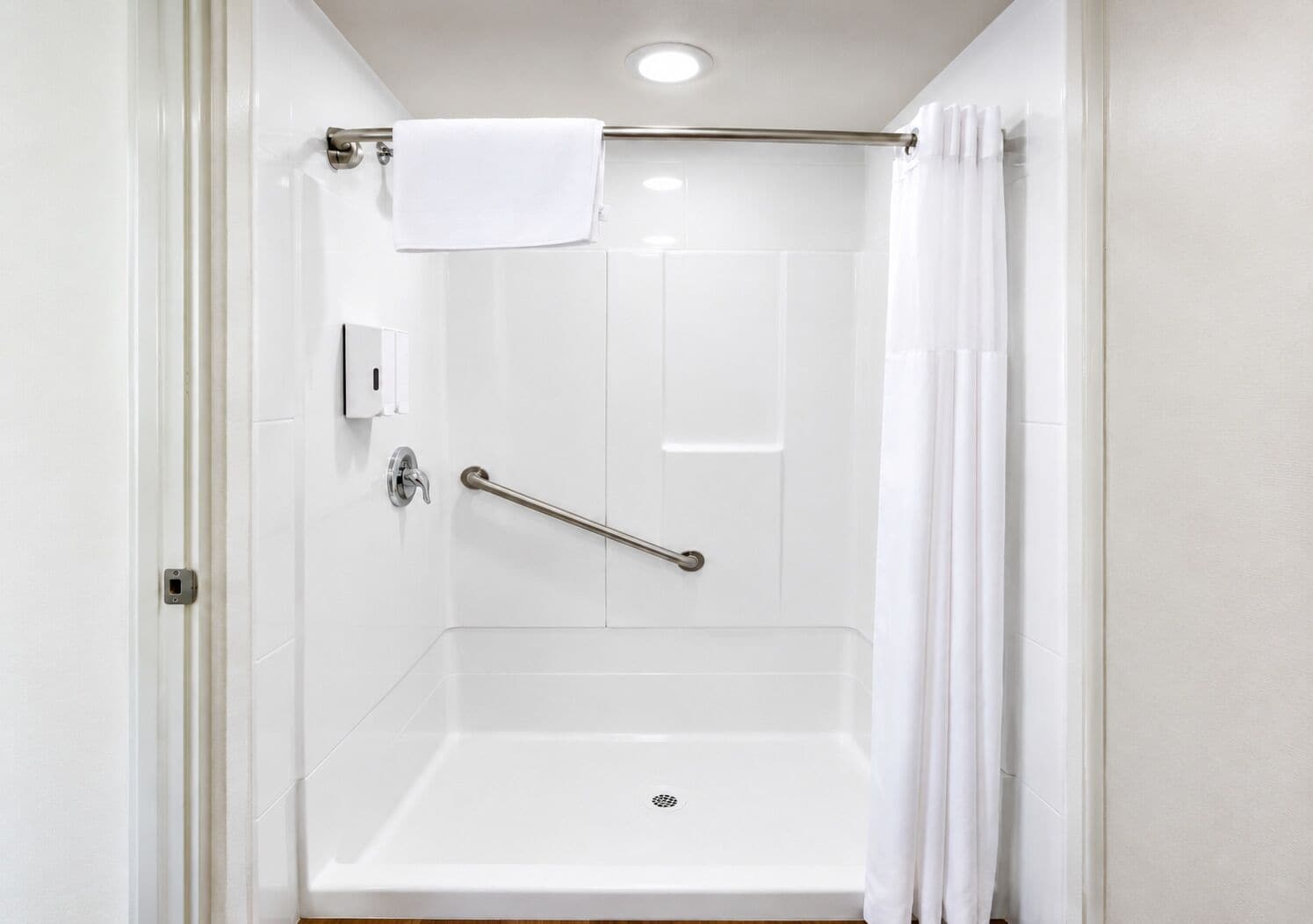Une salle de bain blanche avec une douche, une barre d’appui et un porte-serviettes.