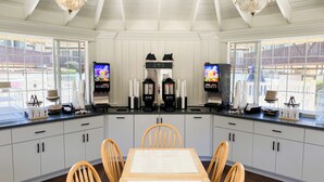 Una cocina moderna con armarios blancos, una mesa de comedor y dos televisores montados en las paredes.