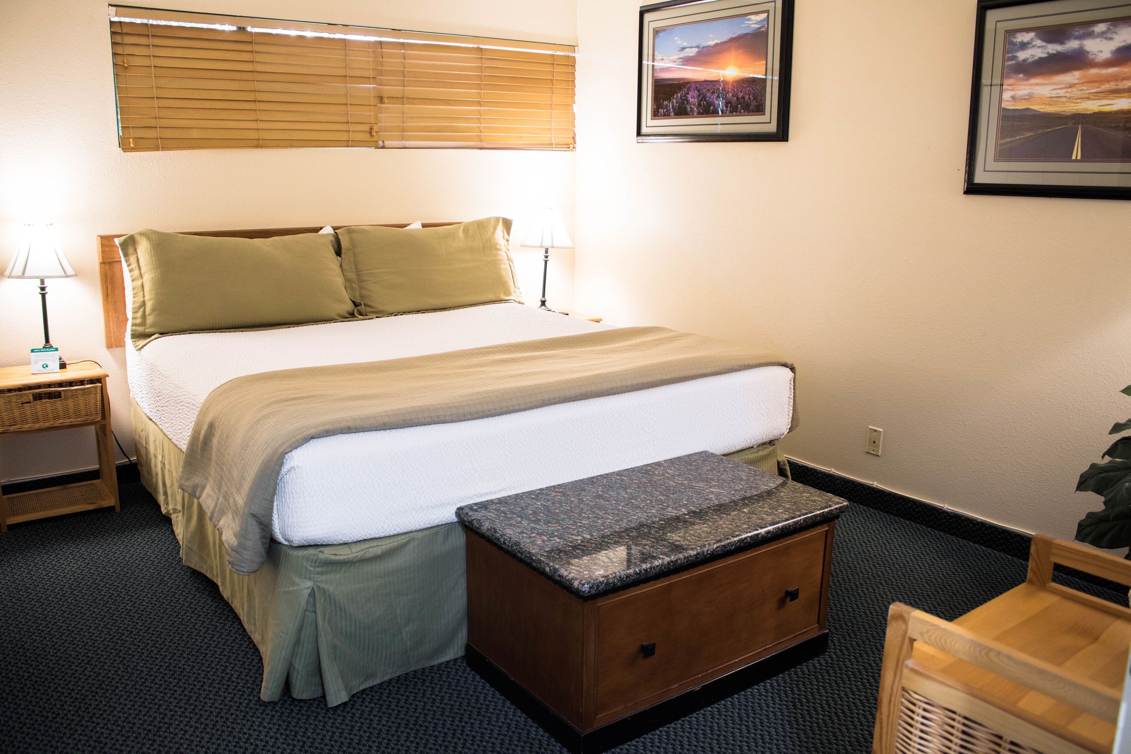 A neatly arranged hotel room with a bed, bedside table, lamp, and a small wooden cabinet.