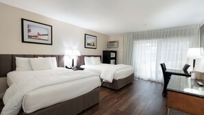 Habitación de hotel con dos camas, un escritorio y una silla. Hay dos cuadros en la pared, una ventana con cortinas y un televisor de pantalla plana también en la pared.