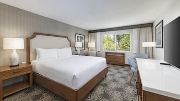 A hotel room with a large bed, bedside tables, a desk, and a window with a view of trees.