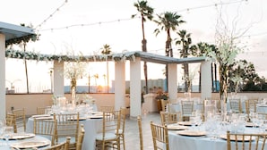 An outdoor dining area with round tables, gold chairs, and string lights. - Redondo Beach Hotel, Tapestry Collection by Hilton (Redondo Beach)