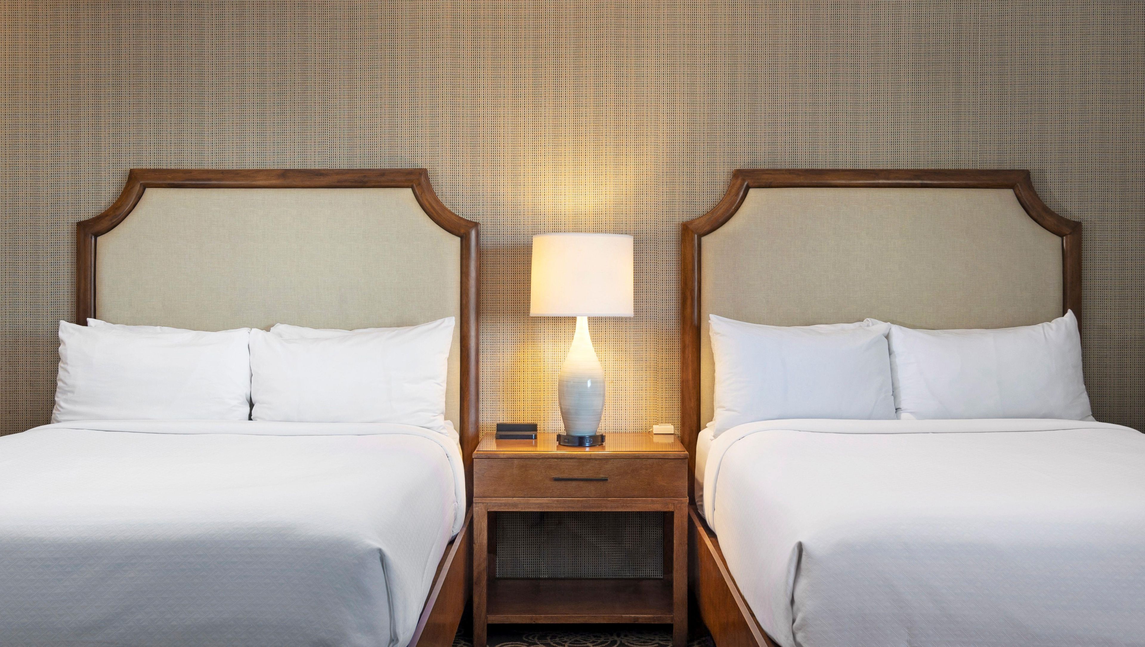 A hotel room with two beds, a nightstand with a lamp, and a wall with a textured pattern.