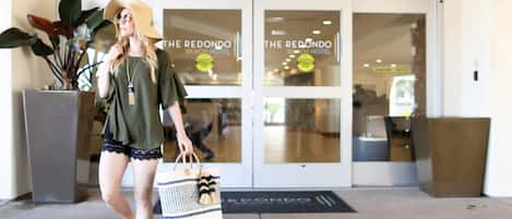 A woman walking towards a hotel entrance with glass doors and a sign reading "The Redondo Beach Hotel".