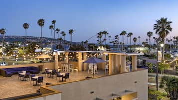 A rooftop terrace with outdoor seating, palm trees, and a view of the cityscape.