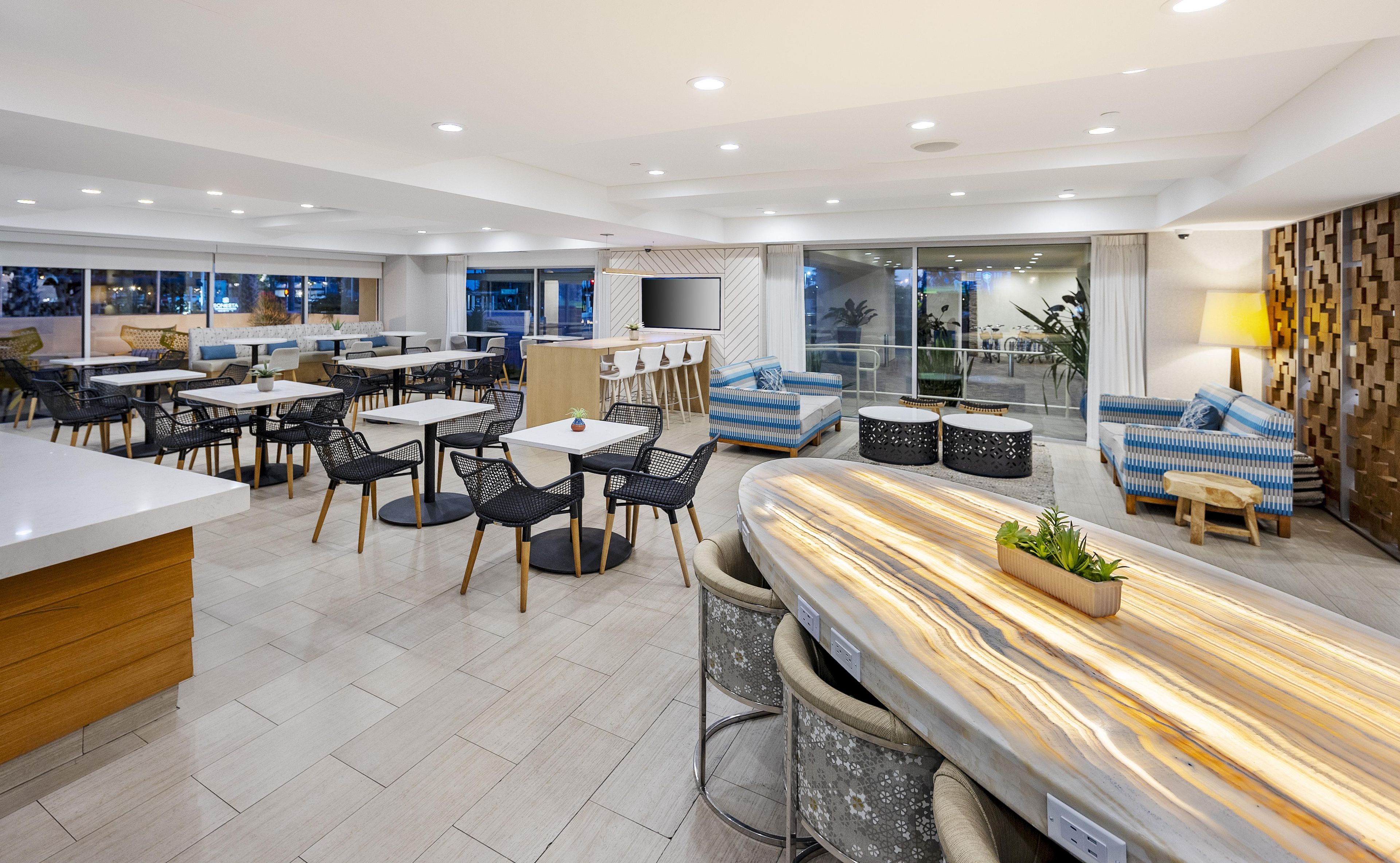 Un espacio interior moderno con una zona de bar, arreglos de asientos y un amplio ventanal con vistas al exterior.