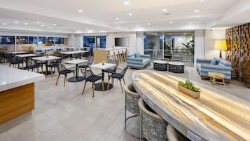 Un espacio interior moderno con una zona de bar, arreglos de asientos y un amplio ventanal con vistas al exterior.
