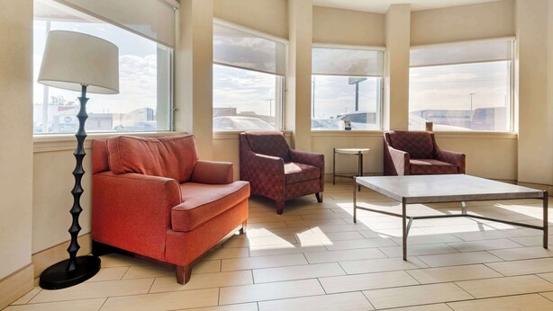Amplia sala de estar con un sofá rojo, dos sillones estampados, una mesita y una lámpara de pie. Grandes ventanas ofrecen luz natural y vistas al exterior.