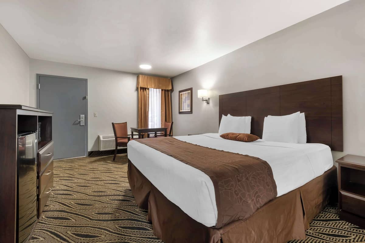 A hotel room with a large bed, a desk, a chair, a TV, and a wardrobe.