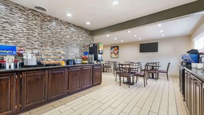 Una barra de desayuno moderna con pared de piedra, una estación de café y una zona de estar con sillas y mesas.