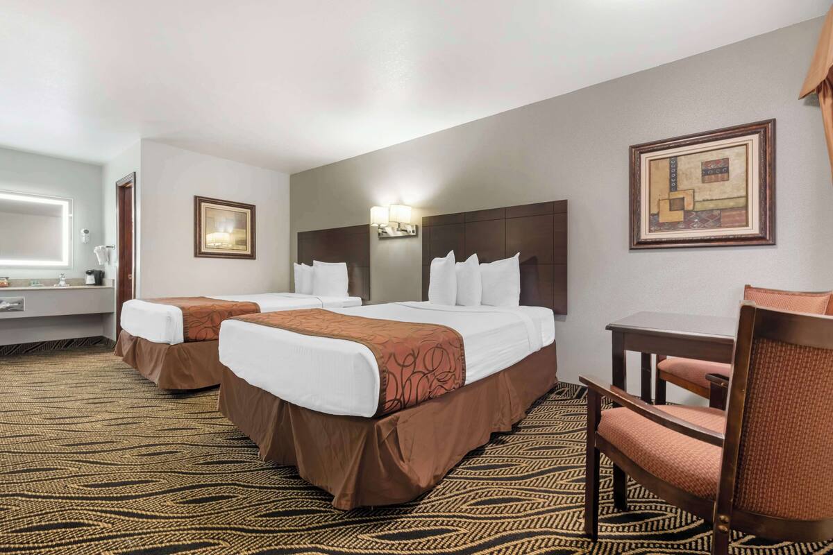 A hotel room with two beds, a desk, and a chair.