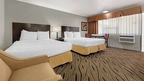 Habitación de hotel con dos camas, un escritorio, una silla y un ventanal con cortinas.