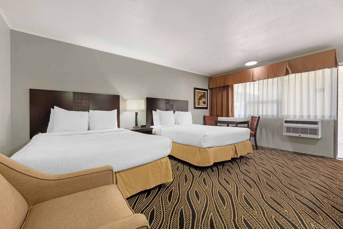 A hotel room with two beds, a desk, a chair, and a large window with curtains.