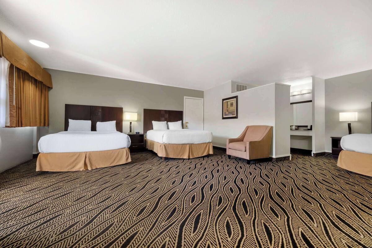 A hotel room with two beds, a chair, and a desk with a lamp.