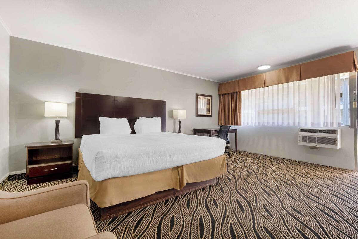 A hotel room with a large bed, a desk, a chair, and a patterned carpet.