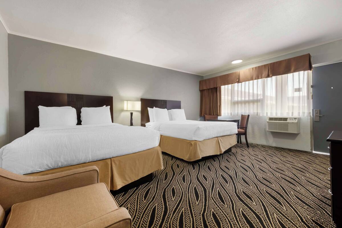A hotel room with two beds, a desk, a chair, and a patterned carpet.