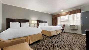 A hotel room with two beds, a desk, a chair, and a patterned carpet.