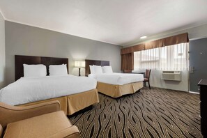 A hotel room with two beds, a desk, a chair, and a patterned carpet.