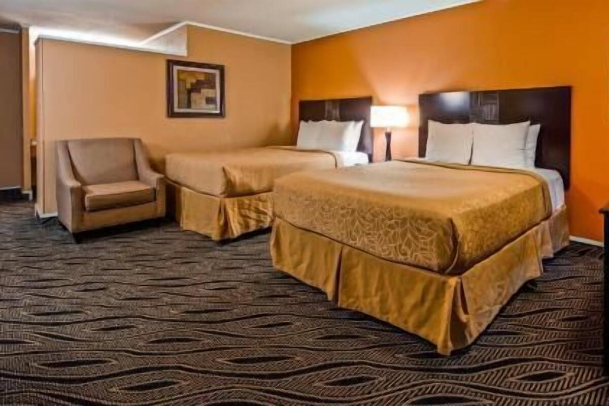 A hotel room with two beds, a chair, and a desk.