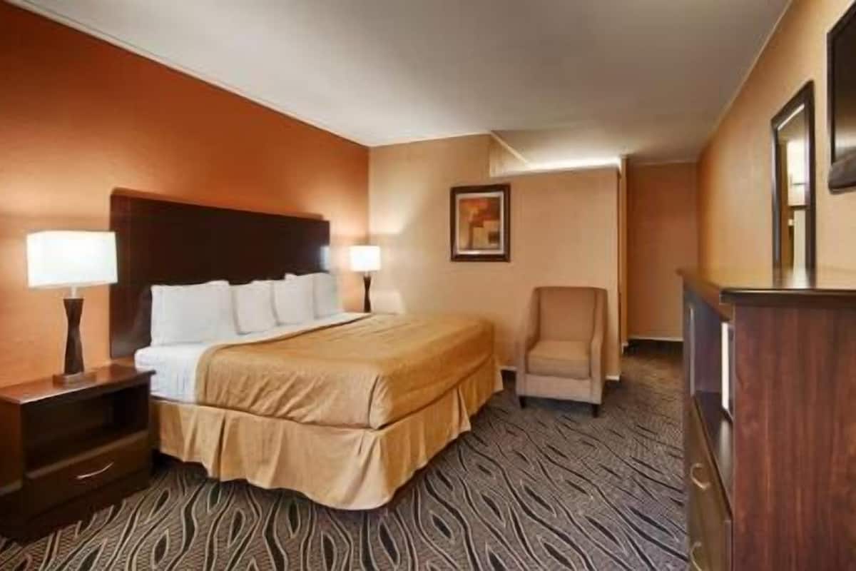 A hotel room with a bed, two bedside lamps, a chair, a desk, and a television on the wall.
