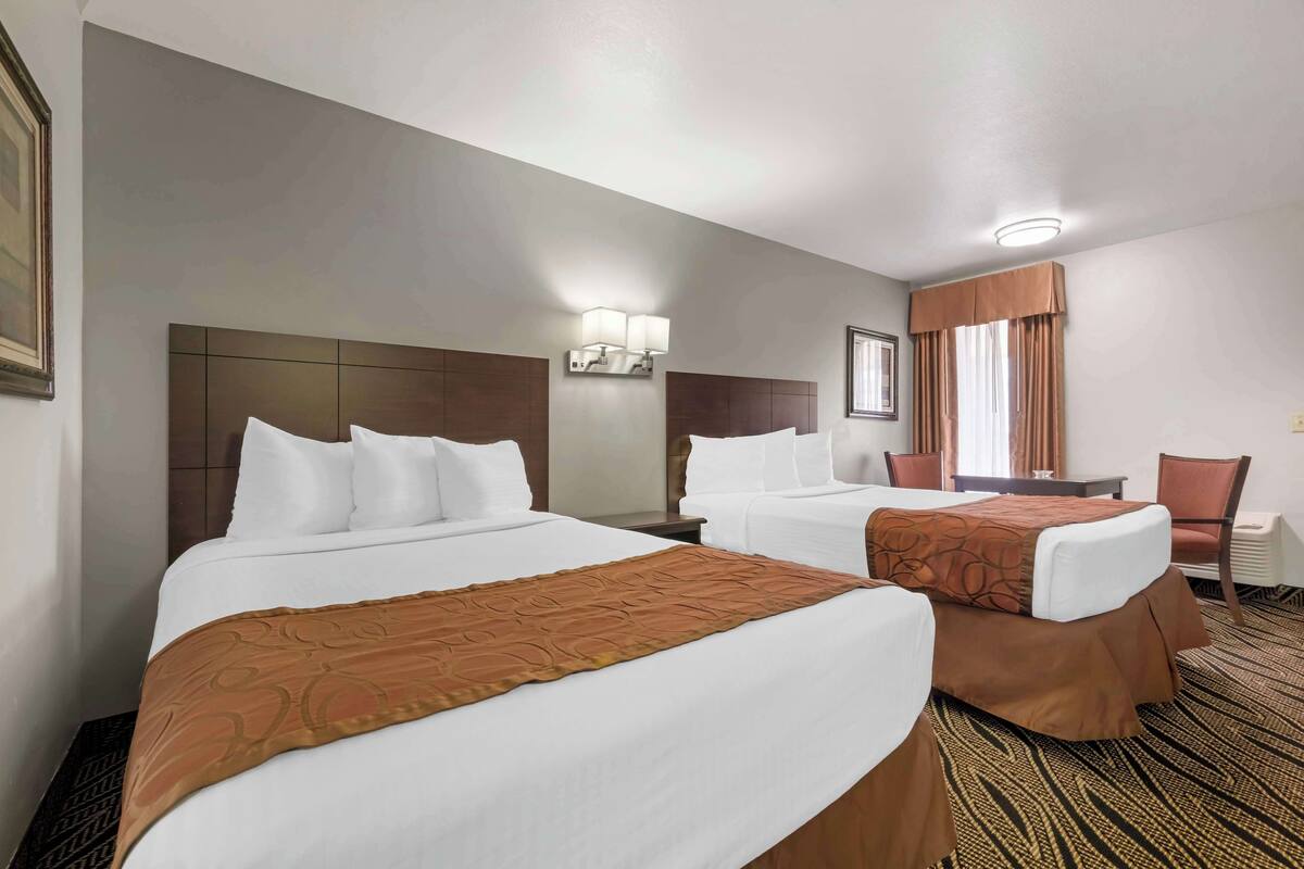A hotel room with two beds, a desk, a chair, and a window with curtains.