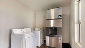 Un lavadero con dos lavadoras Whirlpool y un refrigerador de acero inoxidable con dispensador de agua.