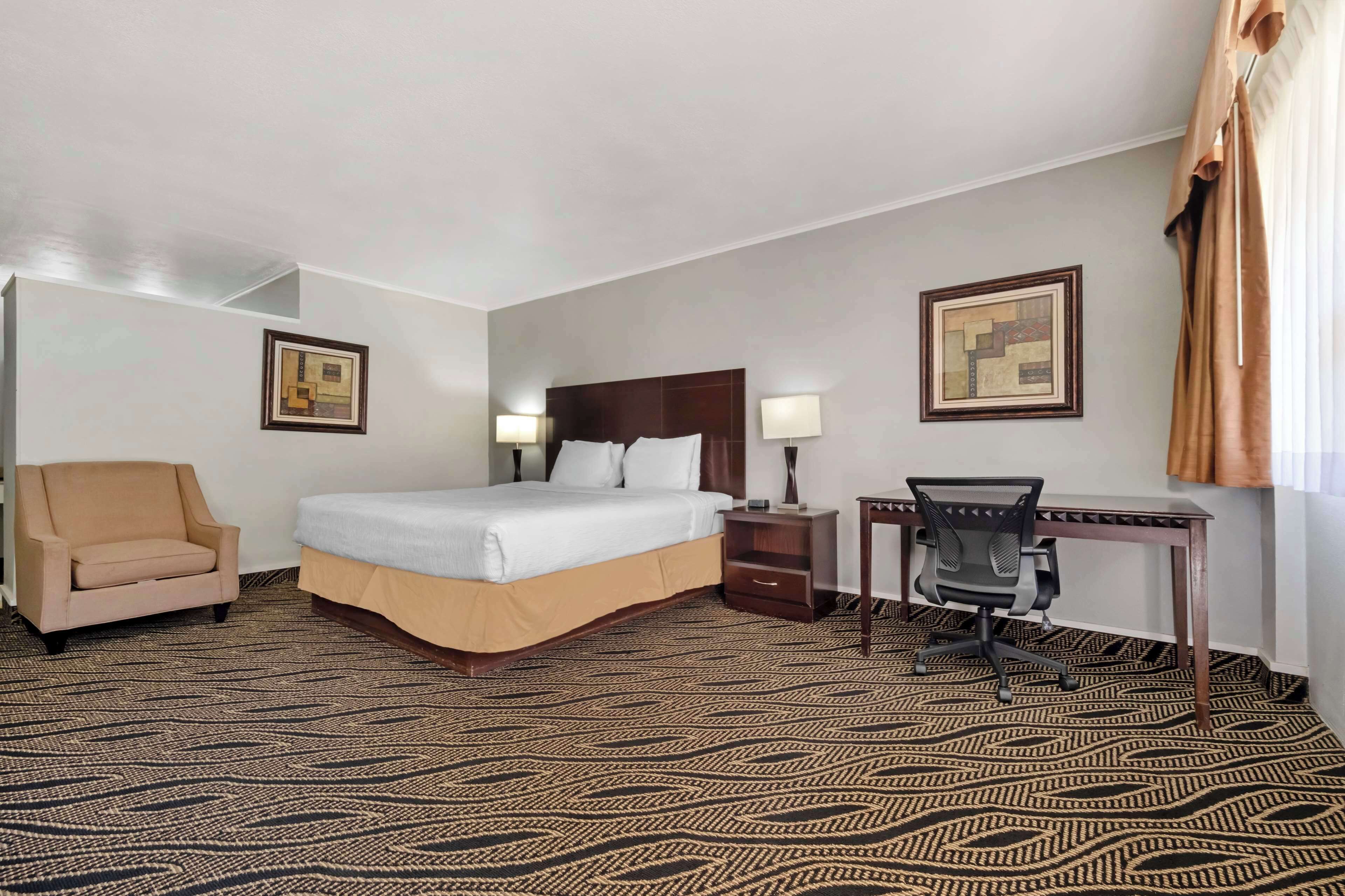 Een hotelkamer met een bed, een bureau, een stoel en twee wandlampen.