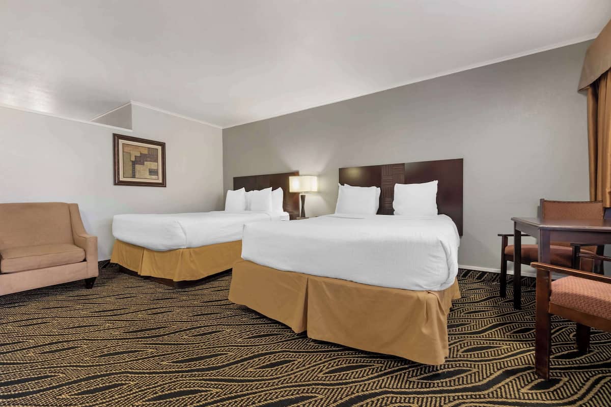 A hotel room with two beds, a sofa, a desk, and a patterned carpet.