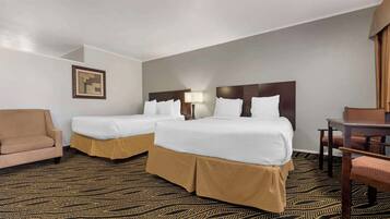 A hotel room with two beds, a sofa, a desk, and a patterned carpet.