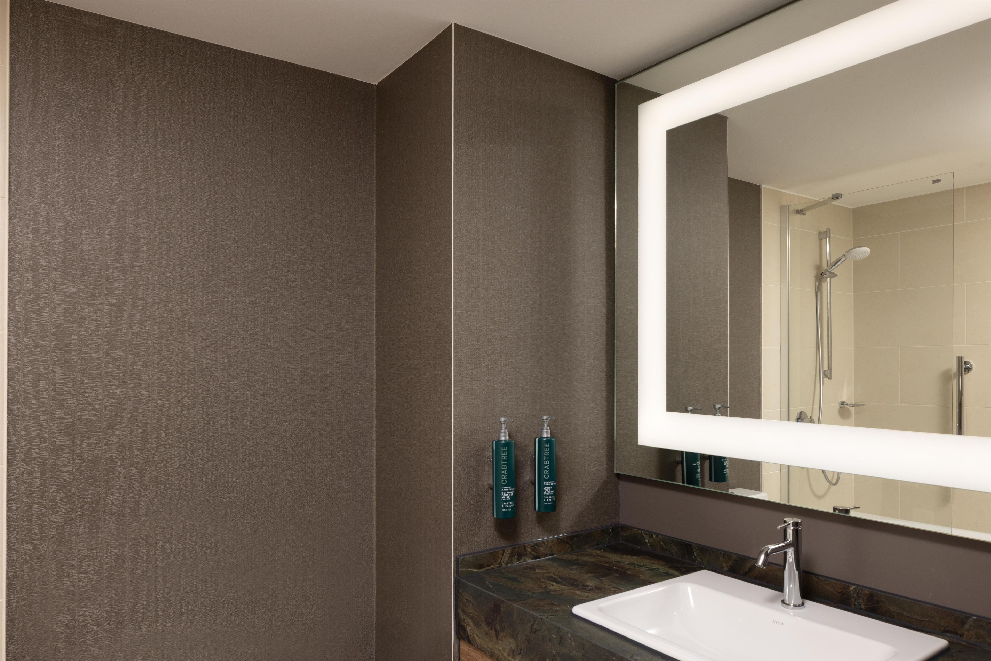 Un baño moderno con un espejo grande, un lavabo y dos botellas verdes en la pared.