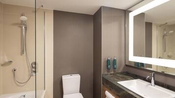 A modern bathroom with a glass-enclosed shower, a white toilet, a large mirror, and a marble countertop.