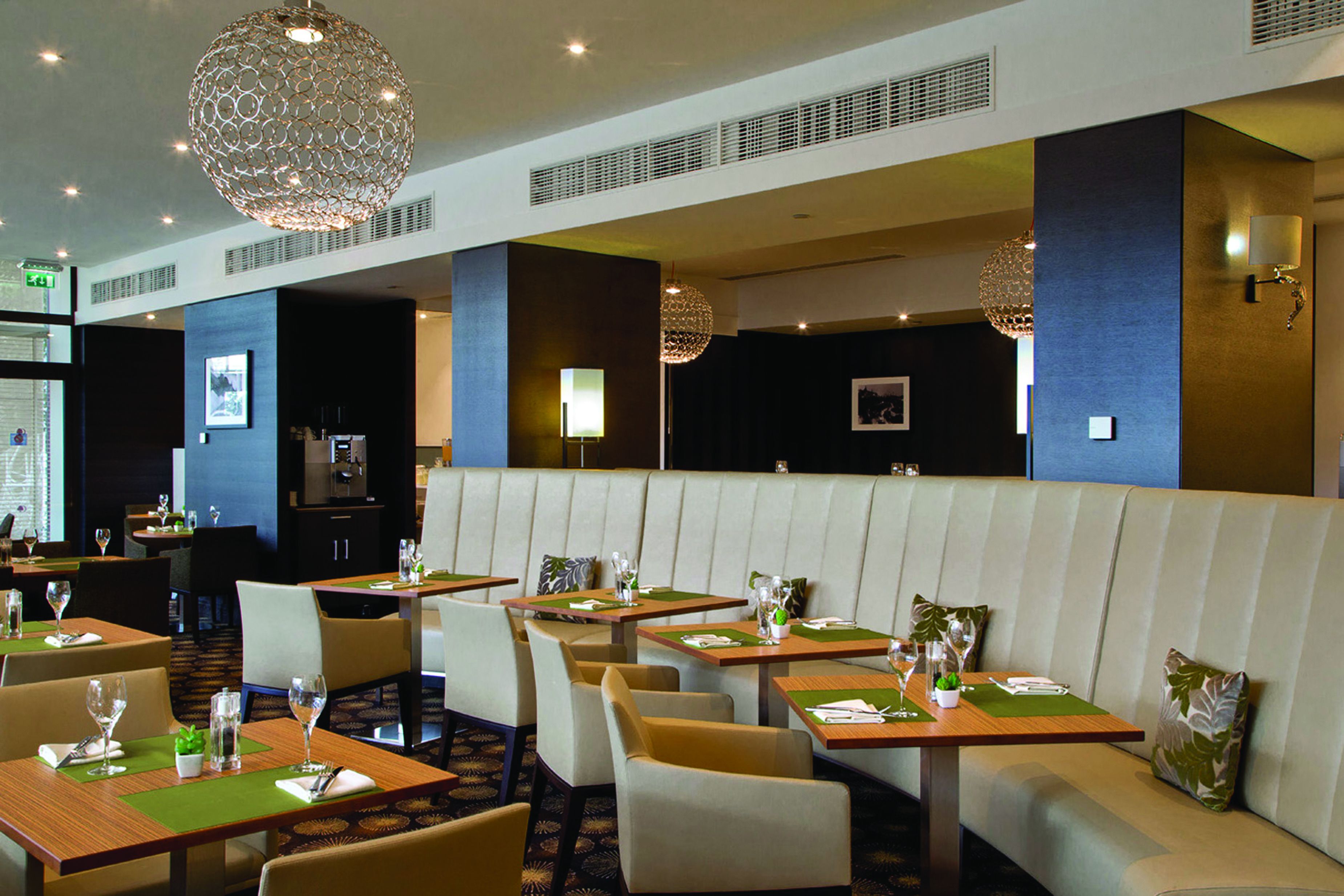 A restaurant with booths and tables, each set with a green placemat, glassware, and a small plant.
