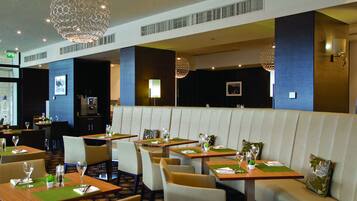 A restaurant with booths and tables, each set with a green placemat, glassware, and a small plant.