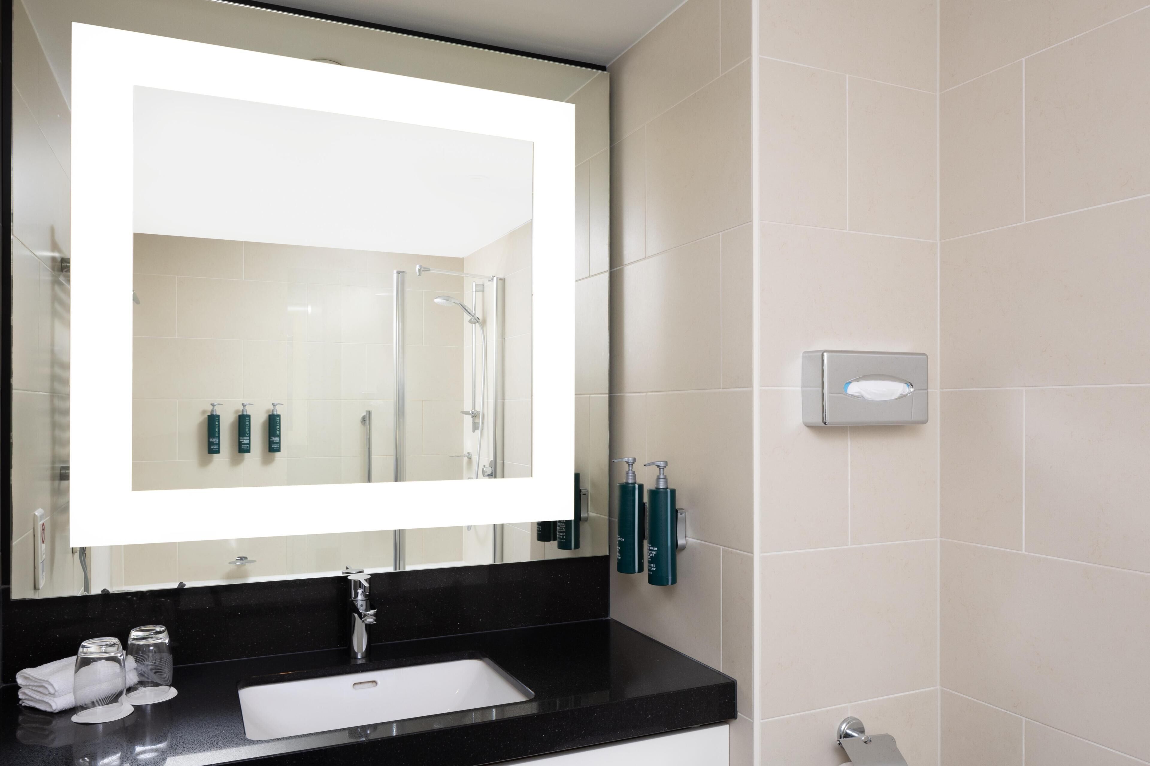 Une salle de bain moderne avec un grand miroir, un plan de toilette noir, un lavabo blanc et des articles de toilette.