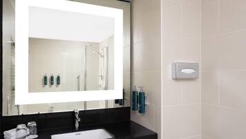 Une salle de bain moderne avec un grand miroir, un plan de toilette noir, un lavabo blanc et des articles de toilette.