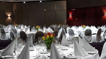 A banquet hall with tables set for a formal event, featuring white tablecloths, neatly arranged silverware, and floral centerpieces.