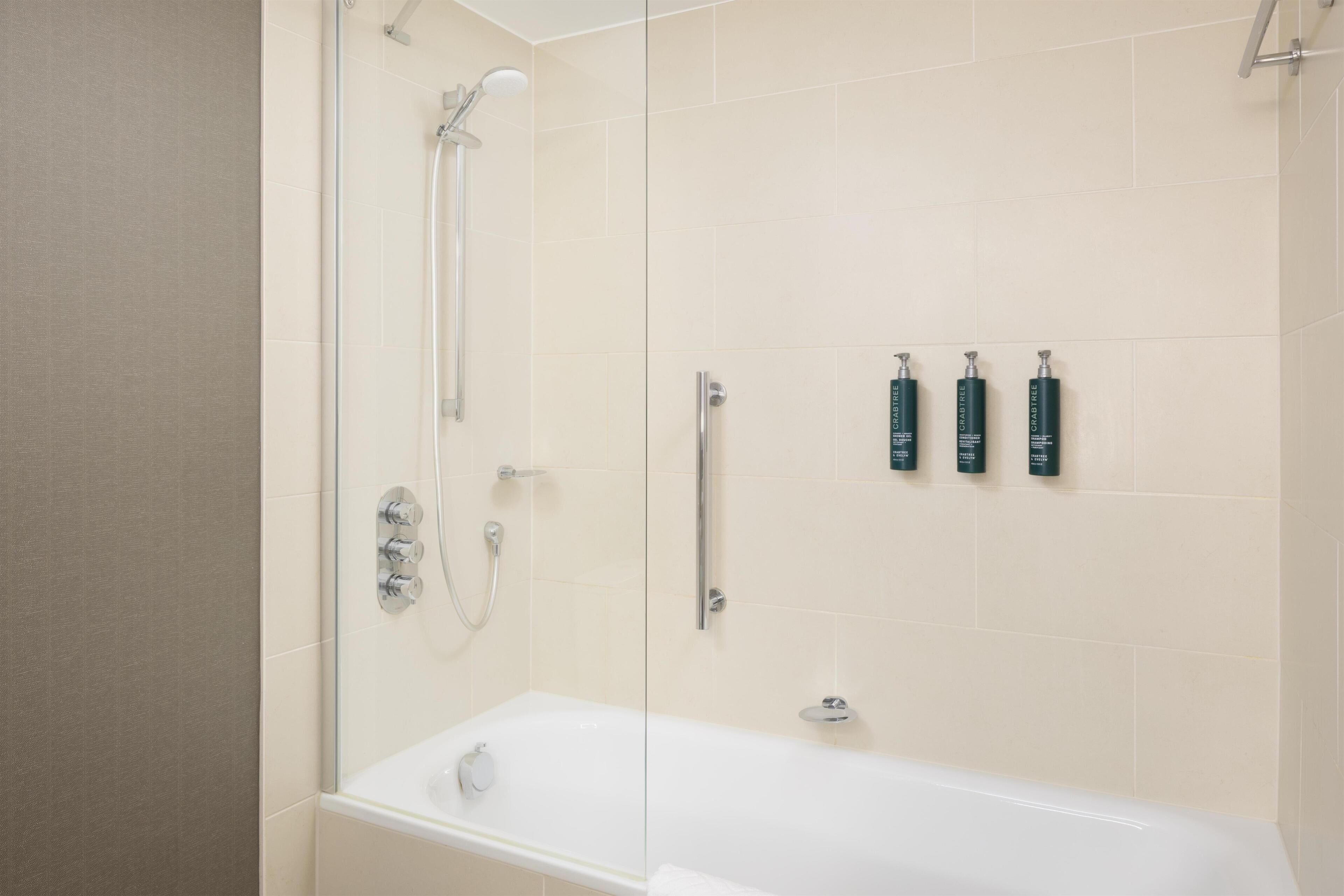 A modern bathroom with a glass-enclosed shower, a white bathtub, and three toiletries on the wall.