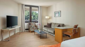Una habitación de hotel con televisión, sofá, sillón, escritorio, lámpara y cama.