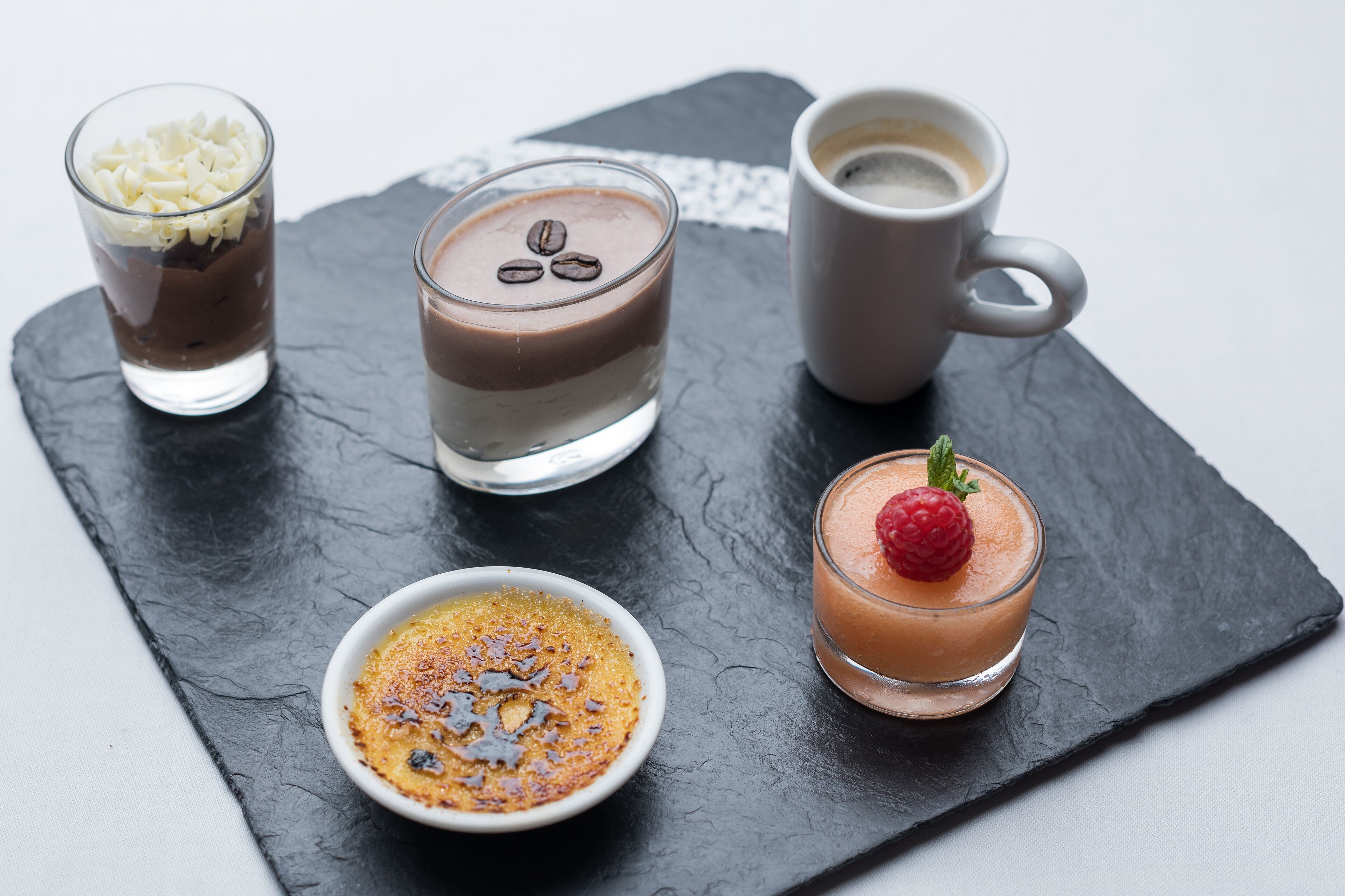 A dessert tray with various chocolate-based treats and a coffee cup on a slate board.