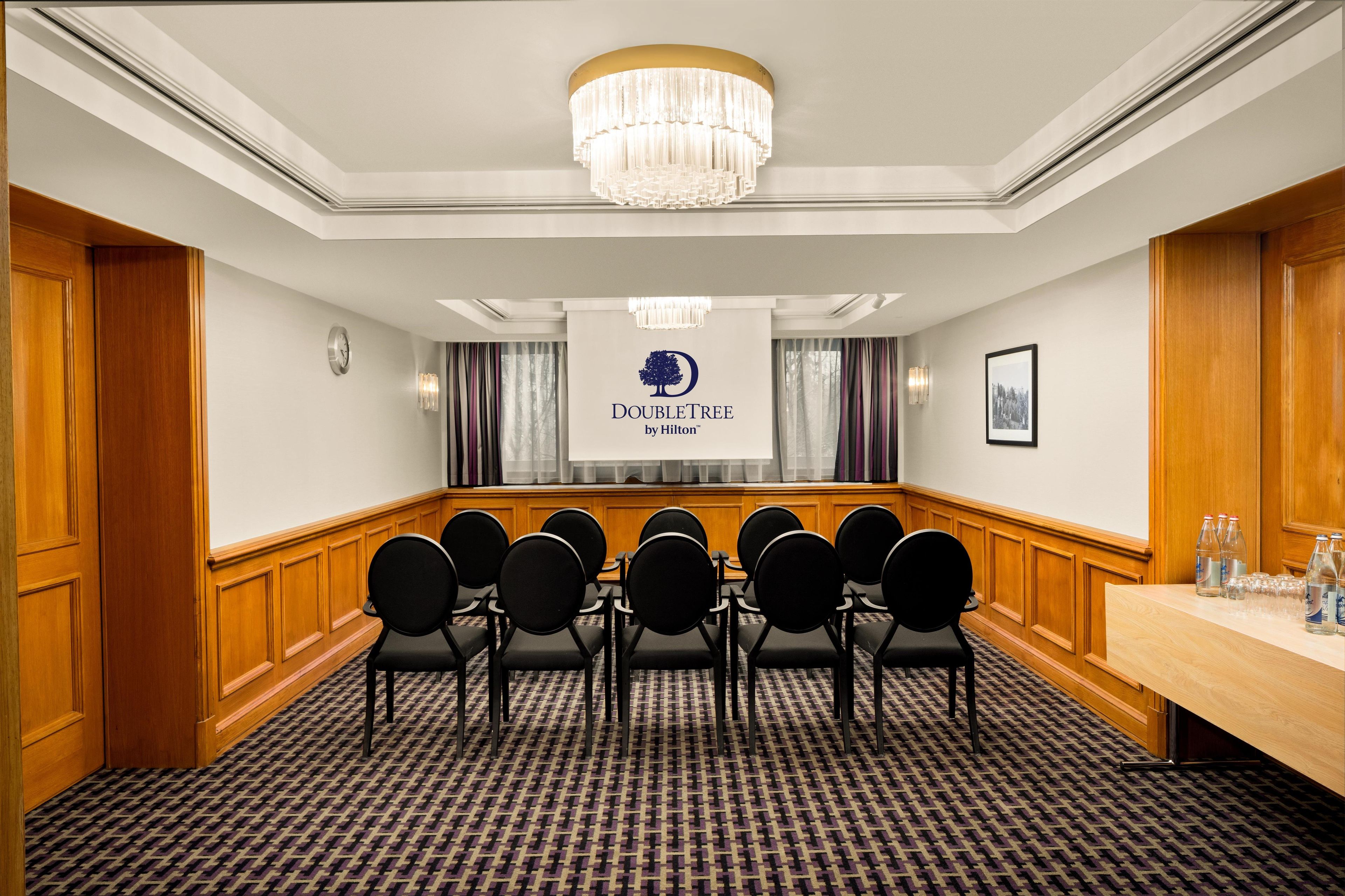 A conference room with a chandelier, a banner with a tree logo, and a row of chairs.