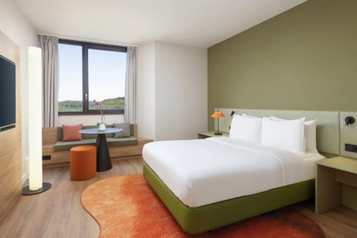 Habitación de hotel con una cama grande, un sofá, una mesita y vistas al exterior.