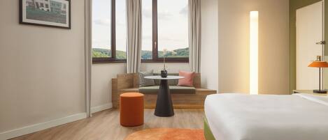 A hotel room with a bed, a round table, a sofa, and a large window with curtains.