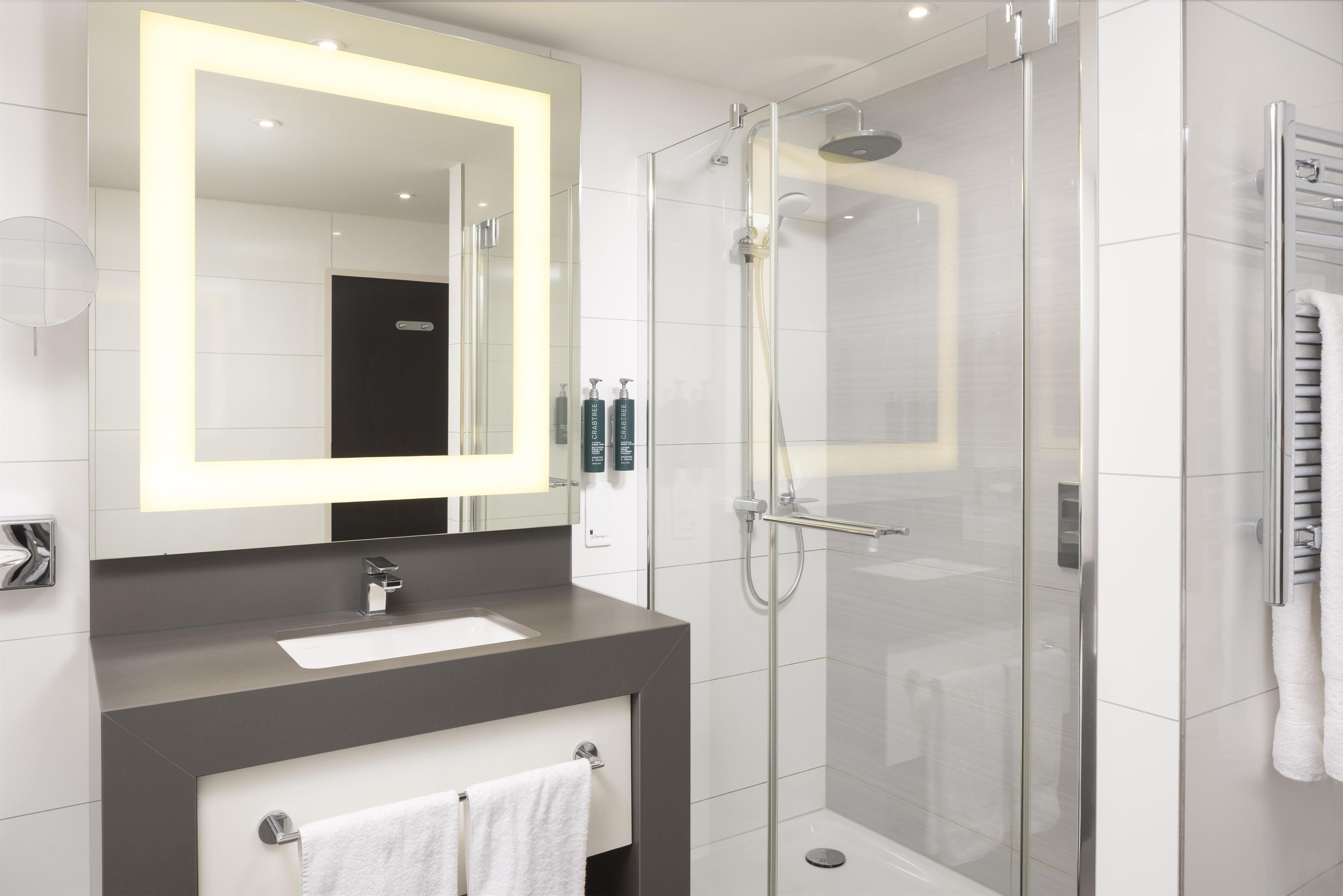 A modern bathroom with a large mirror, a shower enclosure, and a vanity with a sink.