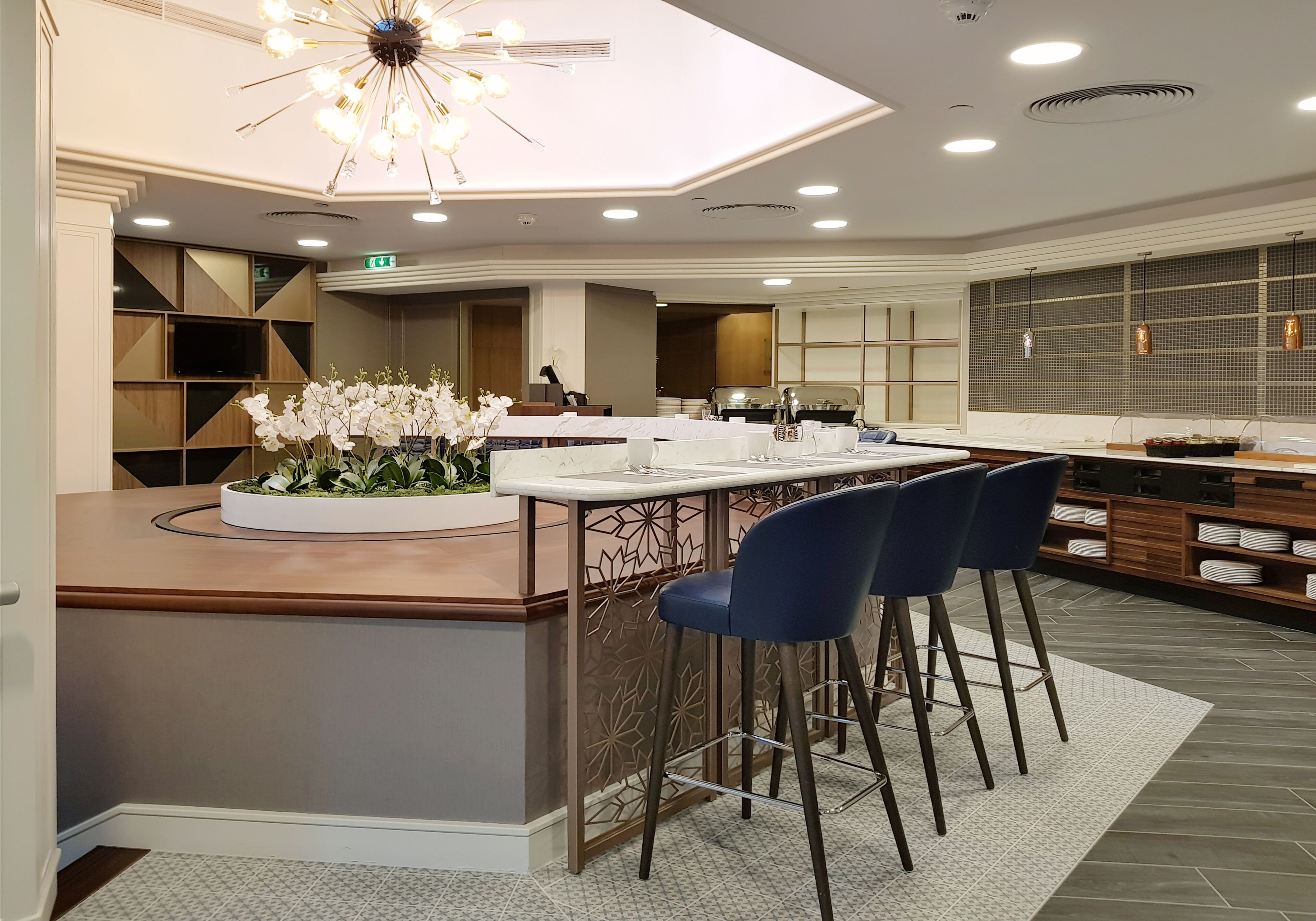 A modern kitchen with a central island, bar stools, and a decorative plant.