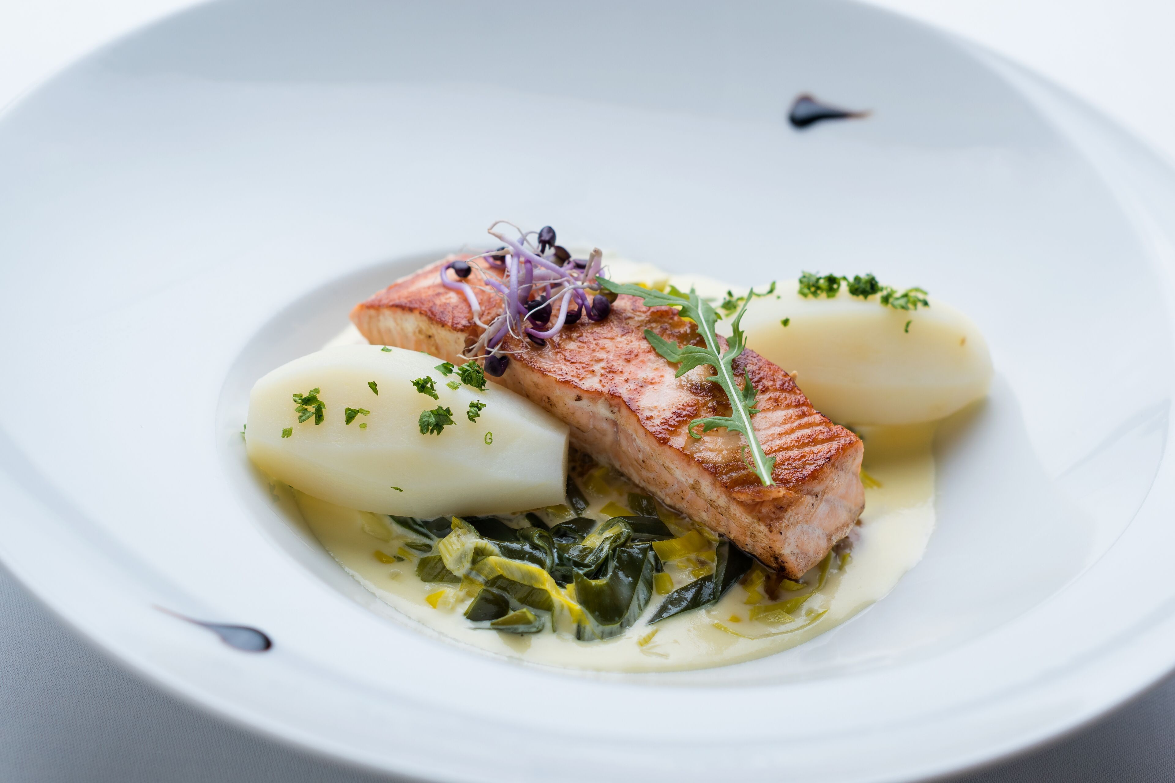 A plate with salmon, potatoes, and greens.