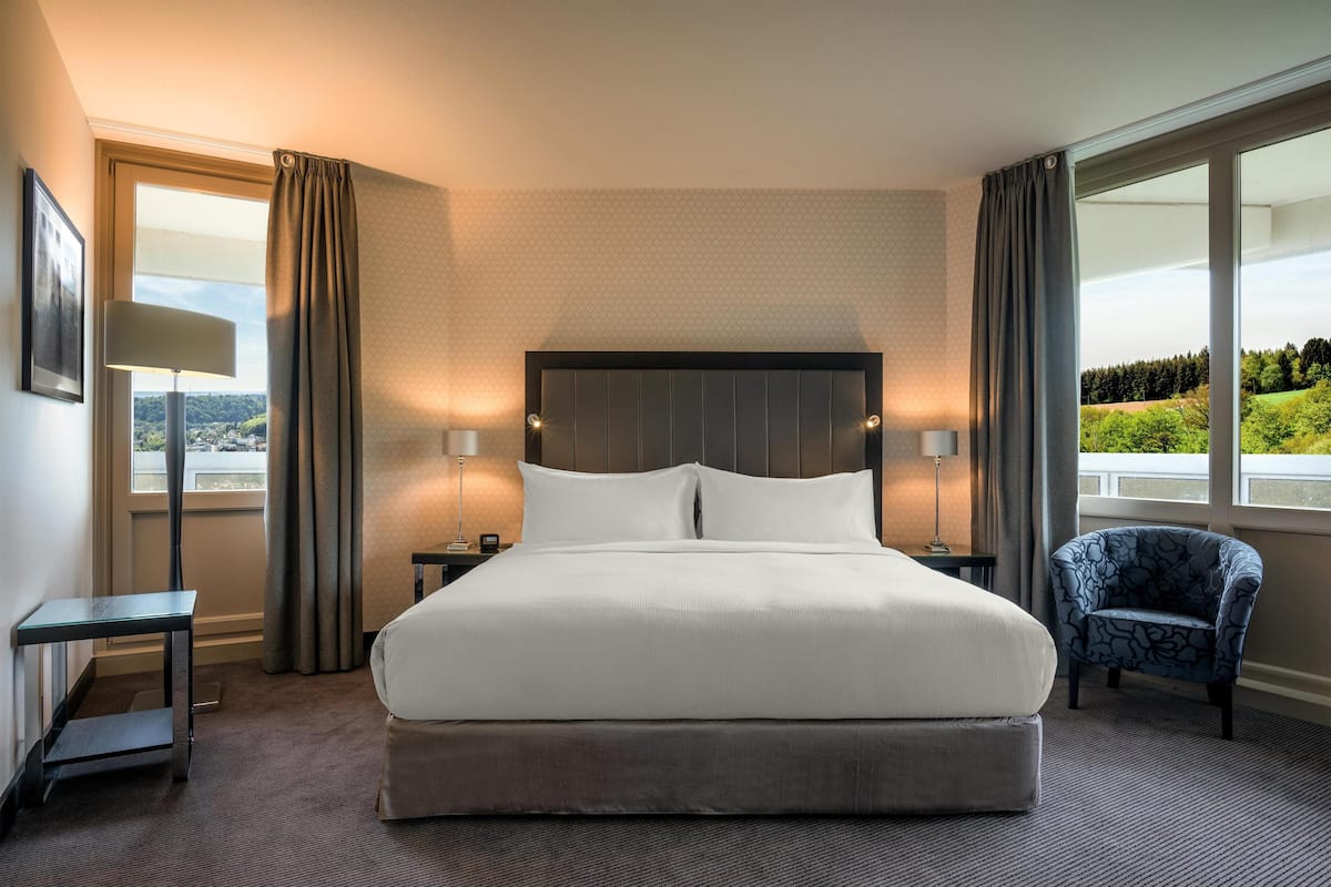 A hotel room with a large bed, two bedside tables, a chair, and a view of the outdoors.